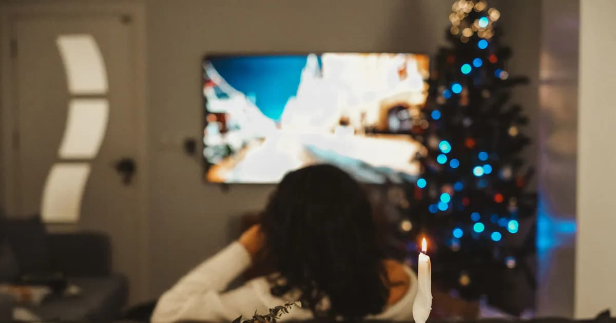 A woman enjoys a cozy evening watching TV by the Christmas tree and candlelight