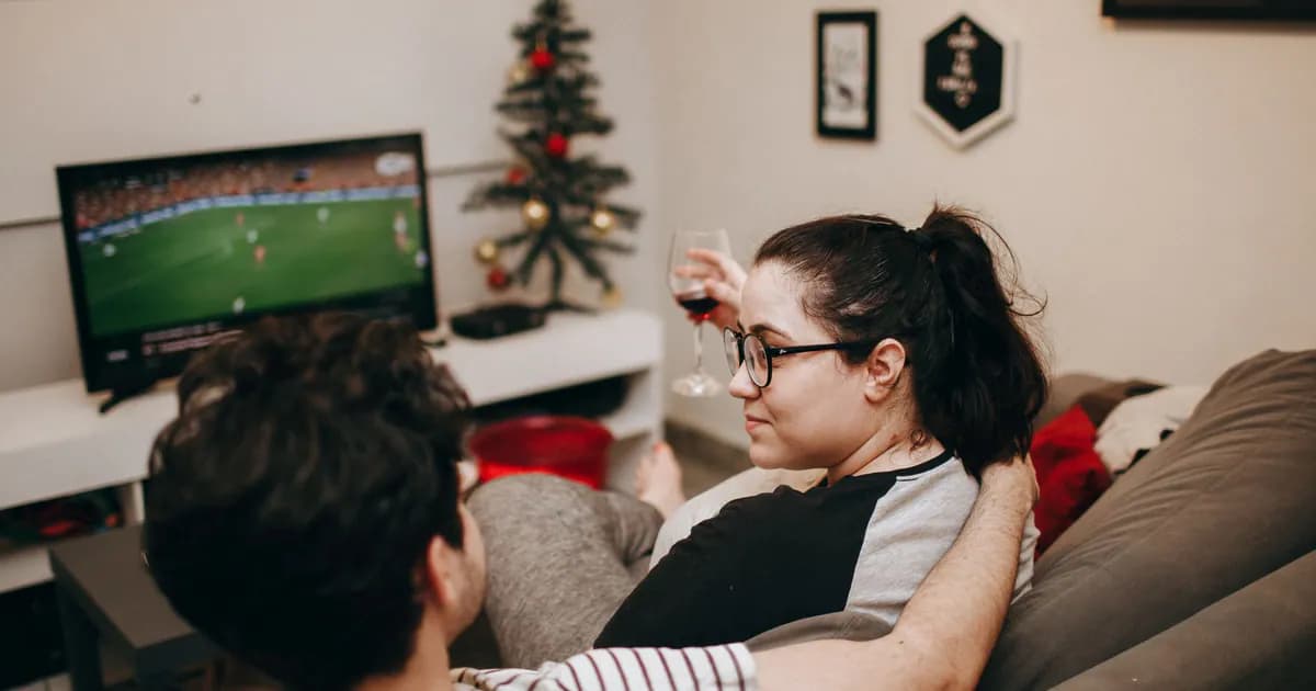 A couple enjoying a cozy evening on the sofa, watching TV with holiday decor in the background