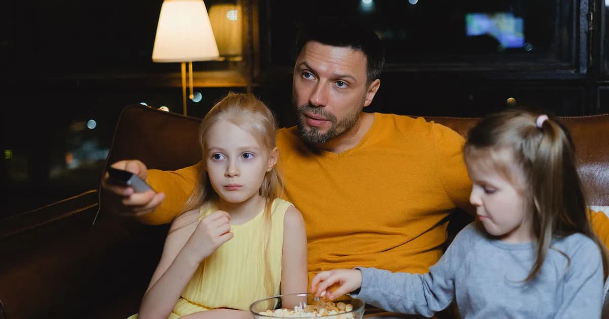 A father and his two daughters enjoying a movie night with popcorn on the couch