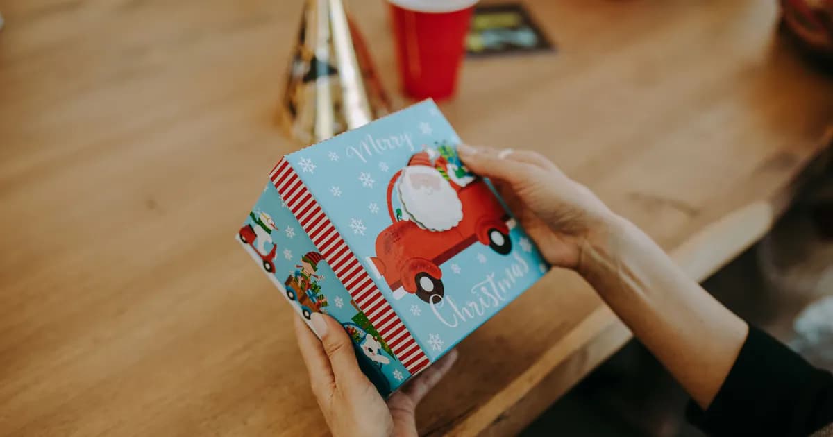 A person holds a colorful Christmas gift box featuring Santa design