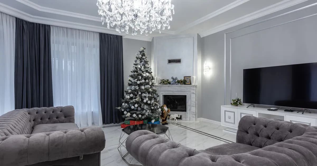 Decorated Christmas tree placed in spacious living room with comfortable sofa and armchair and modern TV set in villa
