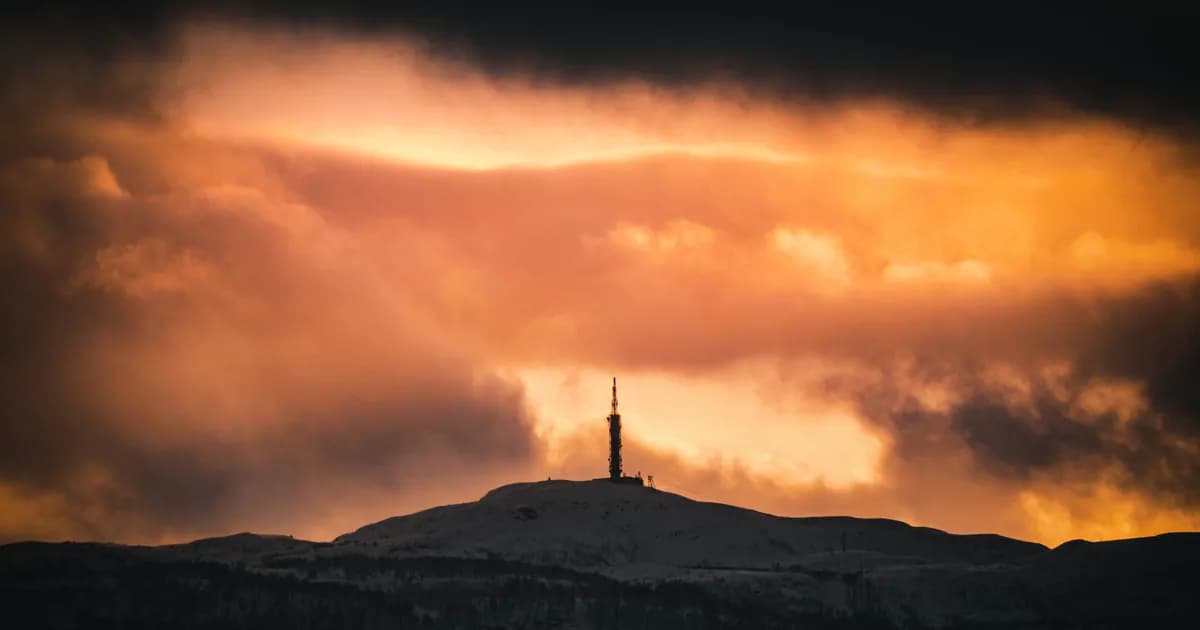 Majestic view of pillar silhouette placed on top of snowy mountain in terrain against glowing sky in dark clouds