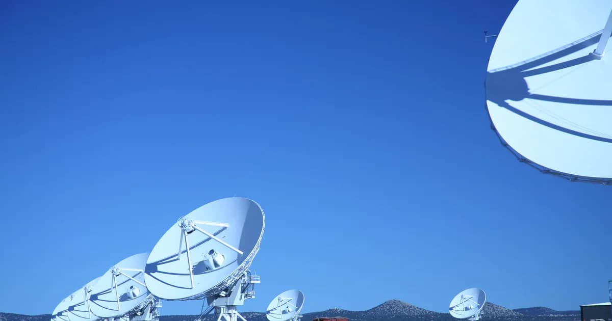 Multiple satellite dishes aligned in a field against a vibrant blue sky