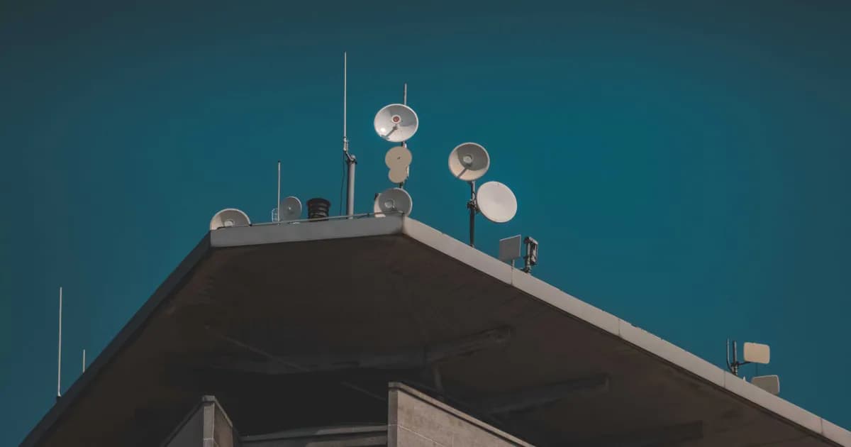 A low-angle view of communication dishes and antennas on a building against a clear blue sky