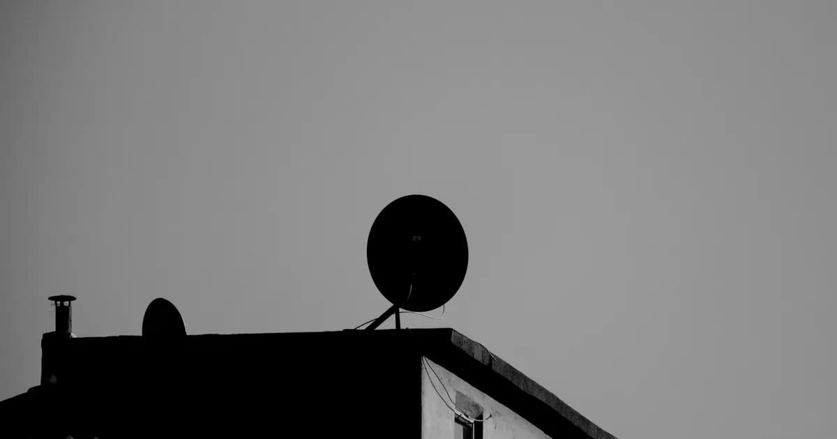 A stark black and white rooftop silhouette featuring a satellite dish against an open sky
