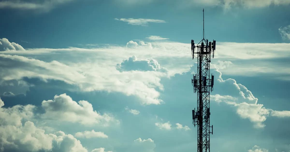 A tall communication tower silhouetted against a bright, cloudy sky