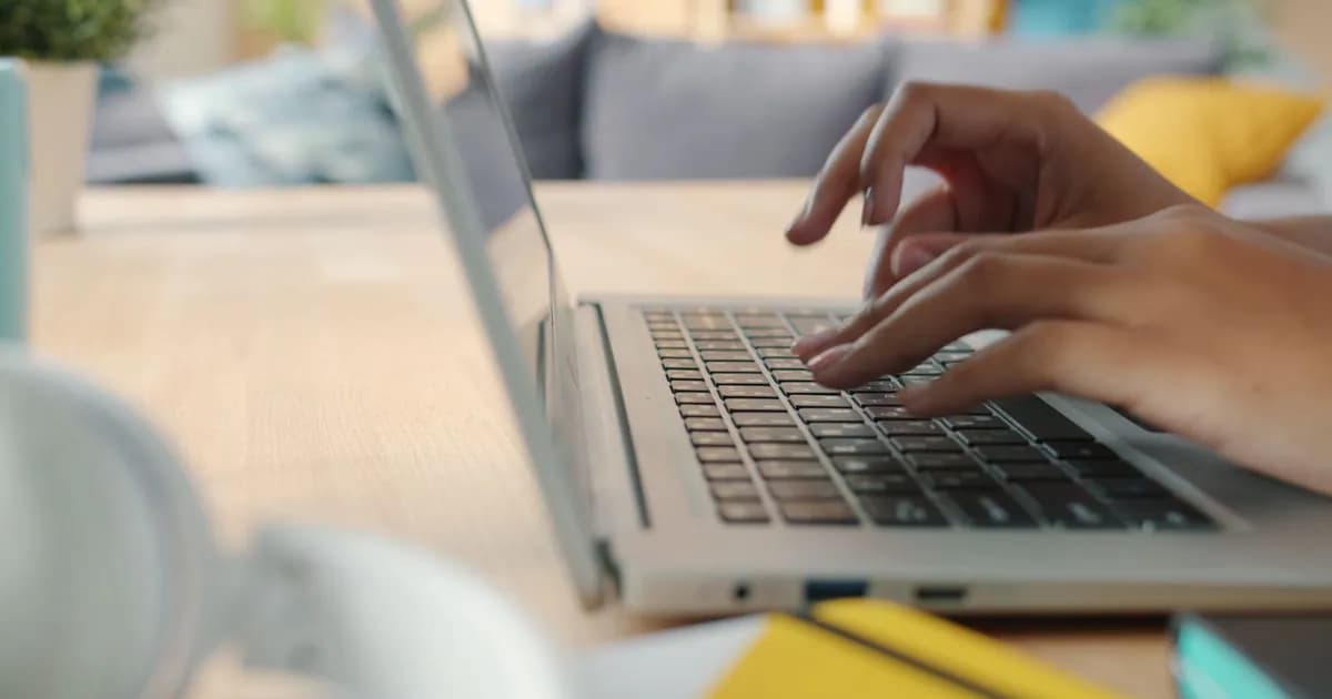 Hands typing on a laptop keyboard indoors with blurred background and natural lighting