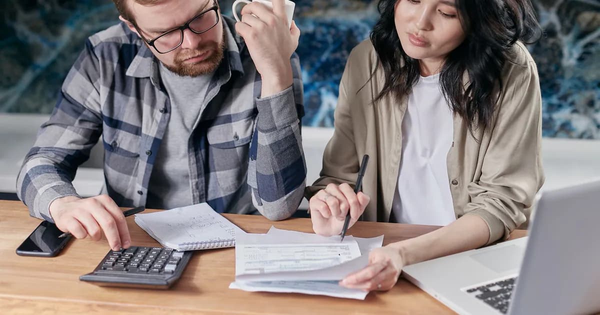 A couple reviewing household bills and budget using a calculator and laptop at their kitchen table