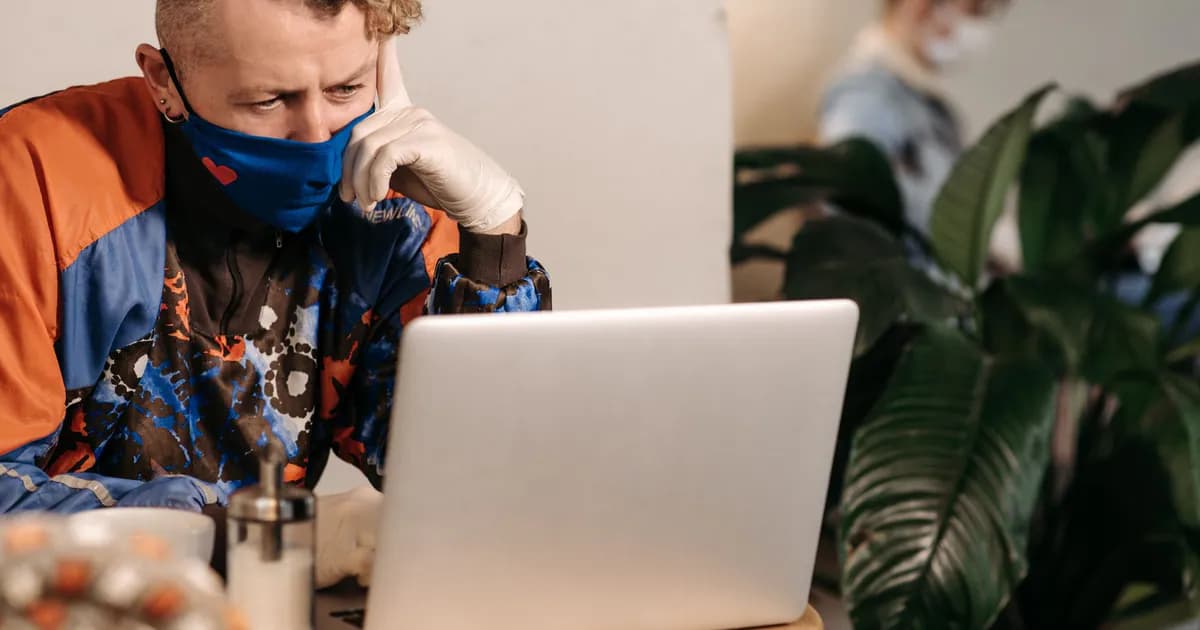 Man wearing a face mask and gloves works on a laptop indoors during the pandemic