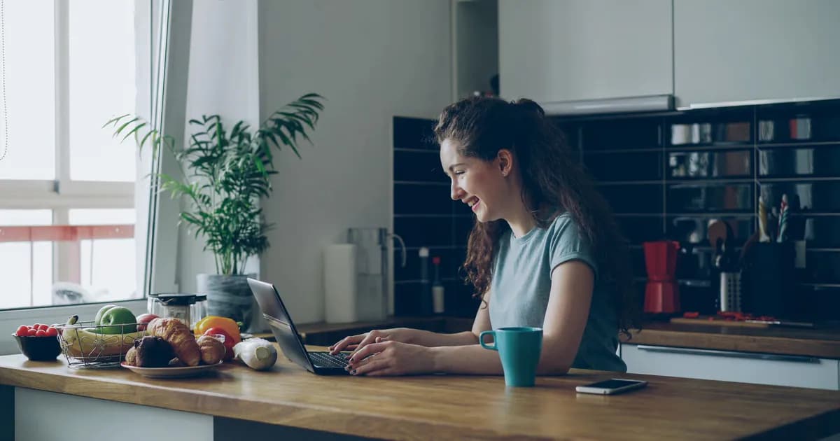 Young woman enjoys working on her laptop in a bright, modern kitchen setting