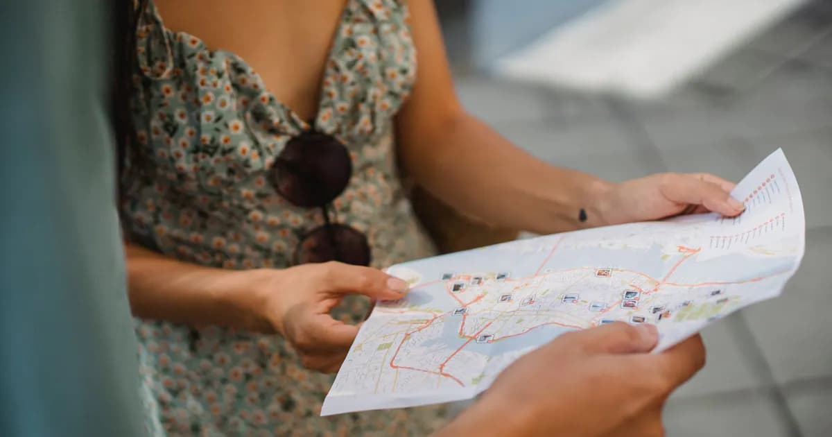 Crop anonymous couple travelers in summer clothes checking location in paper map while walking in unknown city