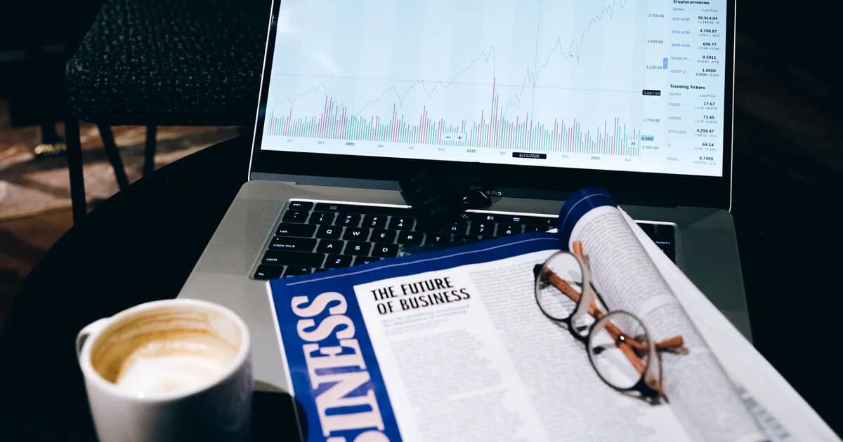 A modern business workspace featuring a laptop showing stock data next to a business magazine and coffee