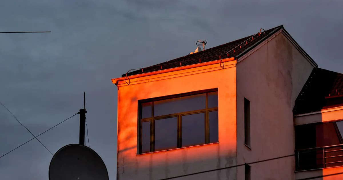 A modern building facade illuminated by sunset light with clouds and a satellite dish