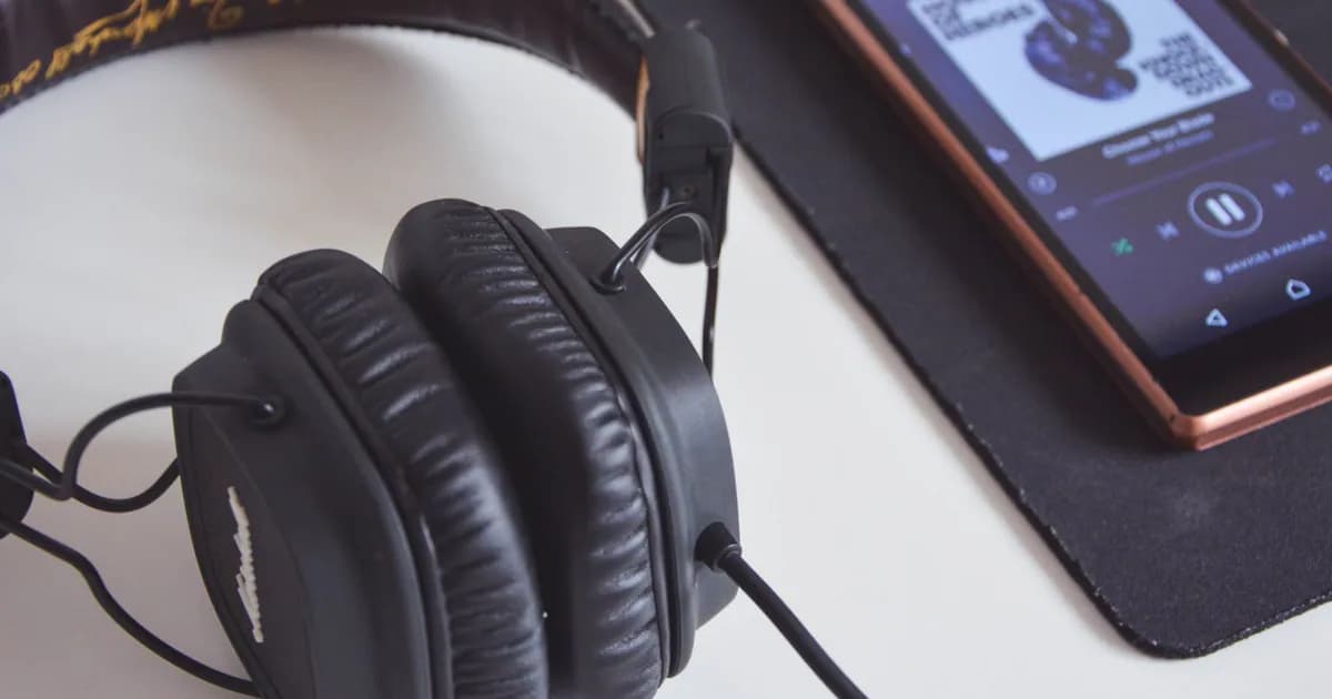 A close-up of headphones and a smartphone playing music on a desk