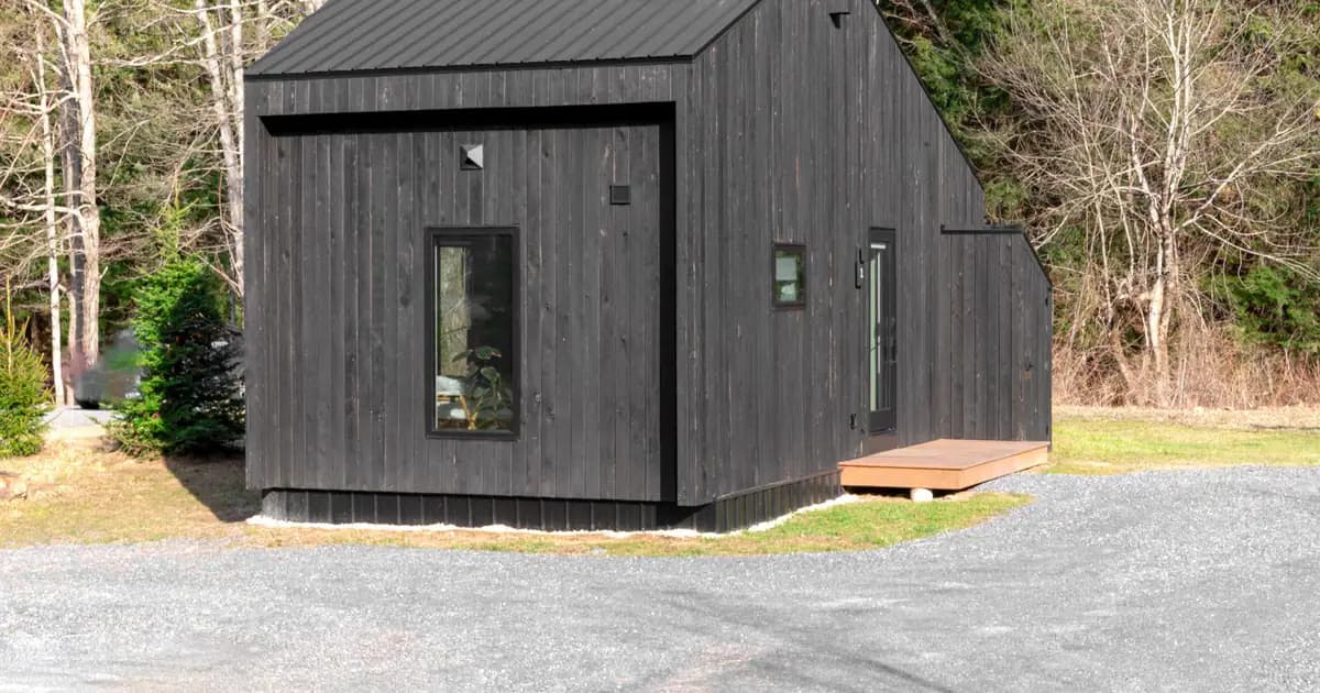 A minimalistic black tiny house nestled in a forest area