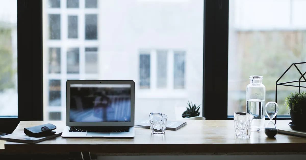 Sleek office desk setup featuring a laptop, glass of water, and open window view