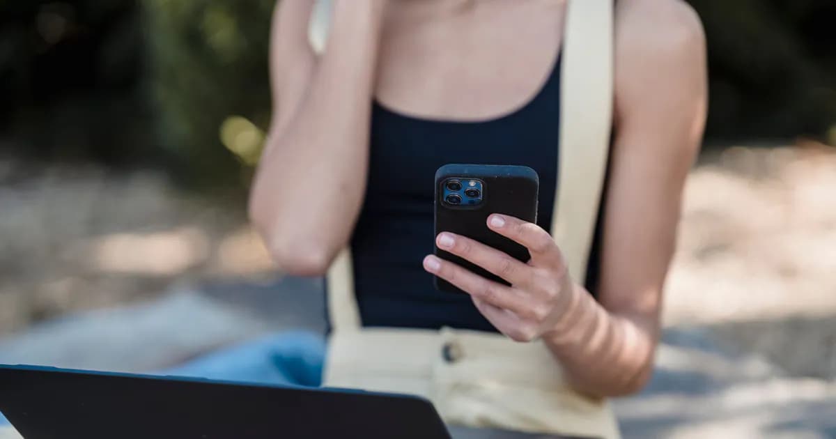 Crop unrecognizable woman with bare shoulders sitting outdoors with laptop and using mobile phone