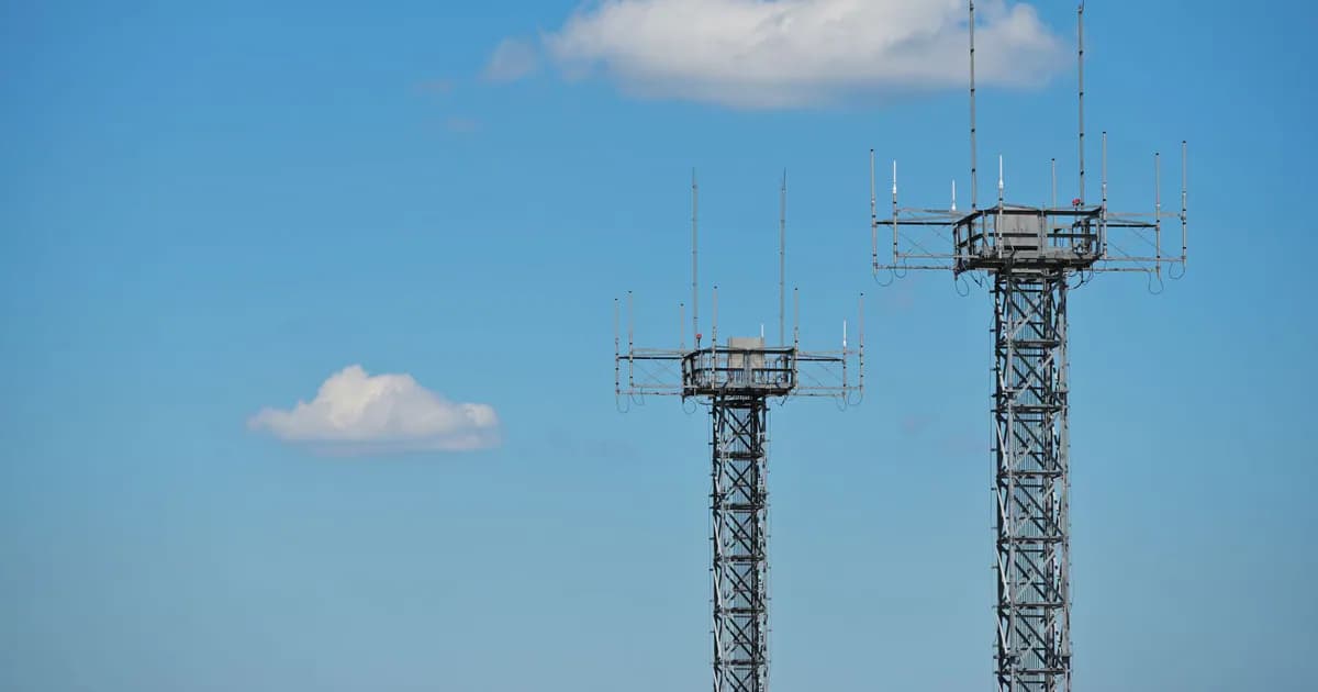 Two telecommunication towers with antennas against a clear blue sky and clouds