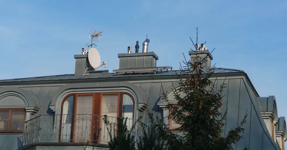 A close-up view of a building roof with antennas and a satellite dish under a clear blue sky