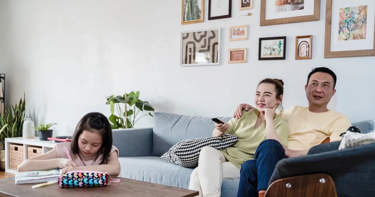 A family enjoying leisure time at home, with a child studying and parents relaxing on the couch