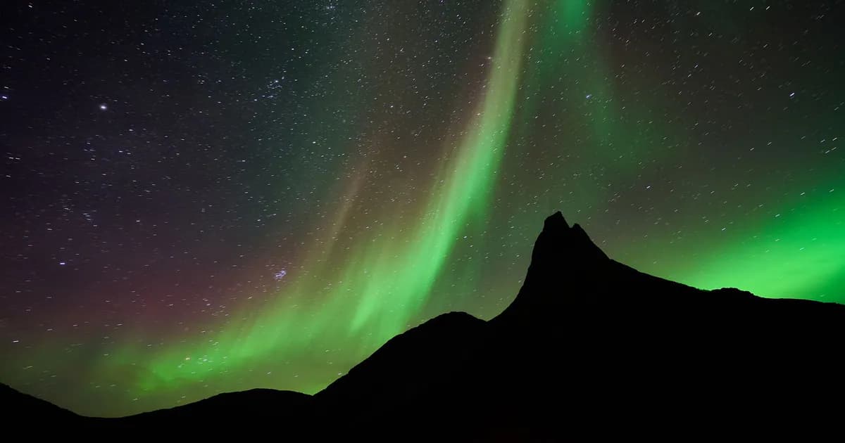 A mesmerizing display of northern lights dancing over a mountainous silhouette and starry night sky