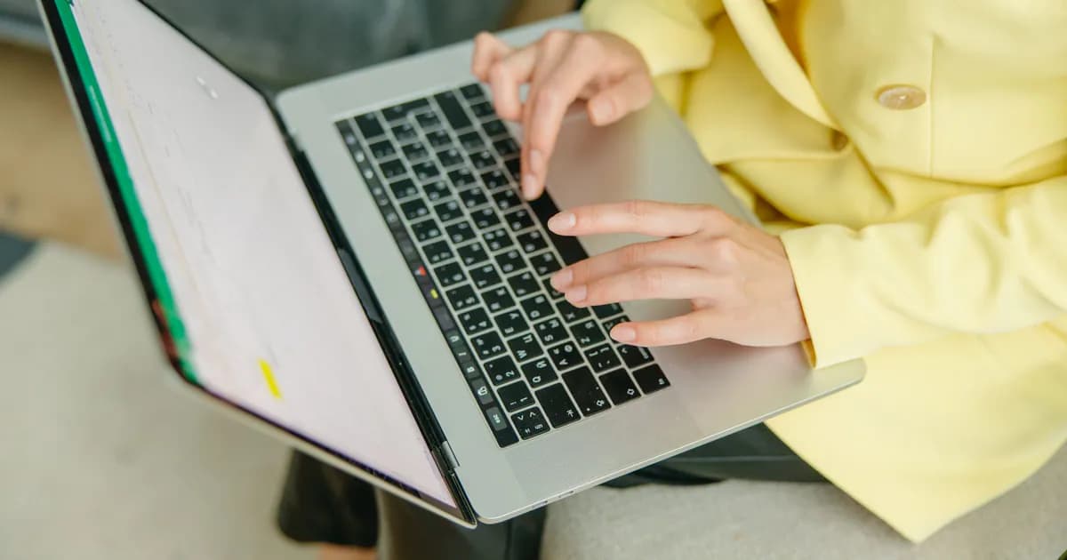 A person in a yellow jacket typing on a laptop indoors. Perfect for depicting work from home or business scenarios