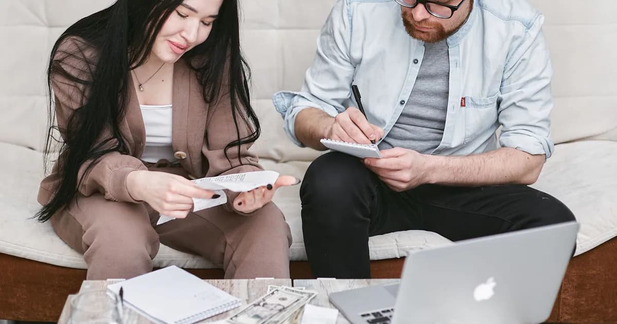 A man and woman sitting indoors, reviewing expenses with notebooks and money on the table