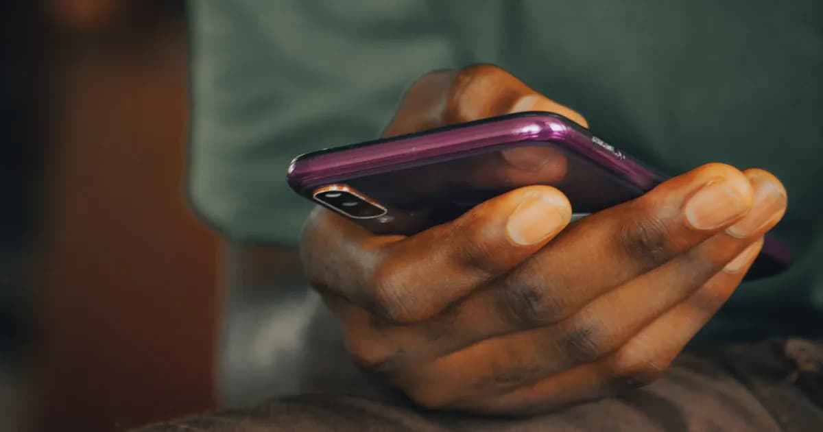 A close-up shot of a person holding a purple smartphone indoors, focusing on texting or browsing