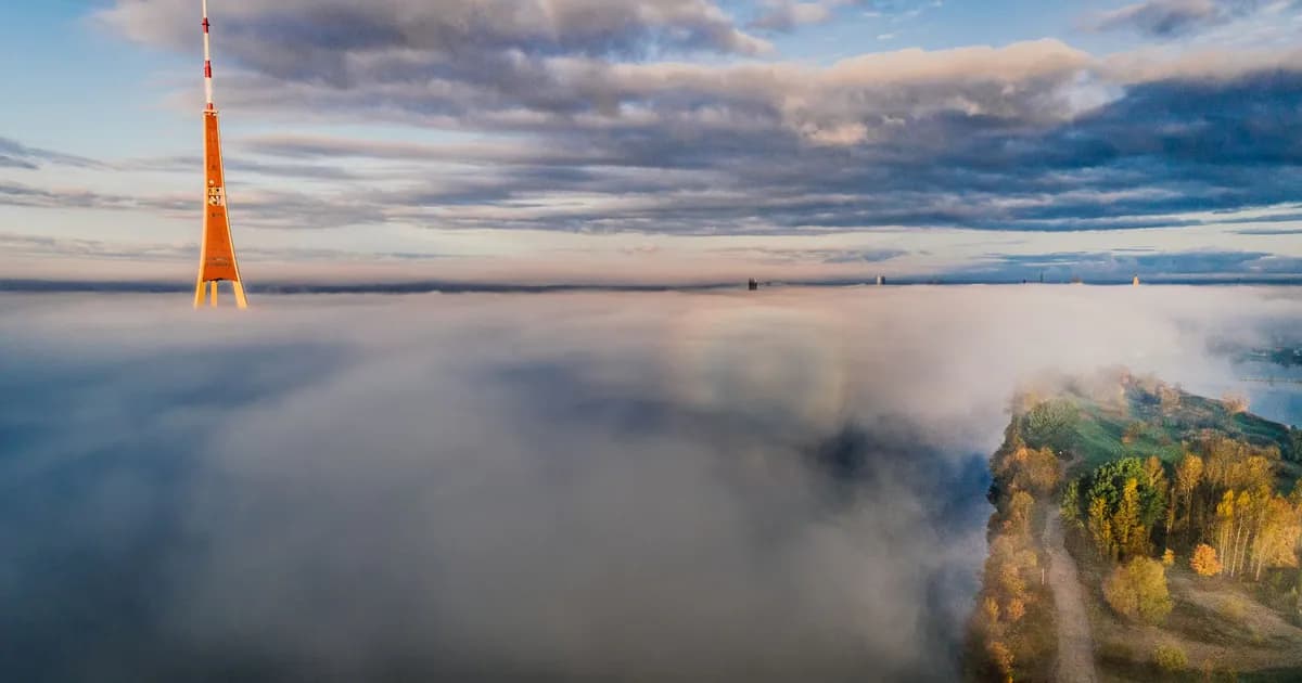 Aerial shot of a tower rising above clouds with a scenic landscape below