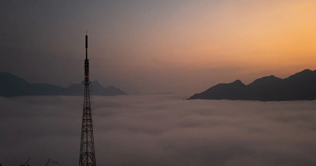 Aerial view of a radio tower amidst clouds at sunrise in a mountainous region