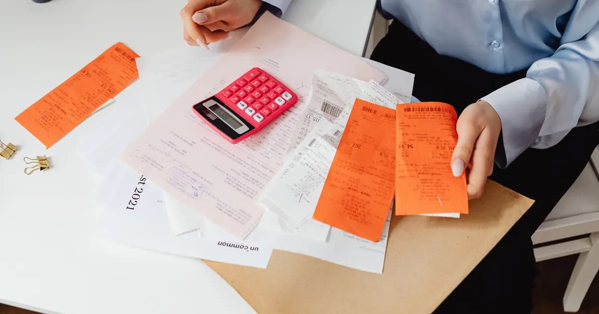 A woman reviews receipts and calculates expenses at a desk with a pink calculator