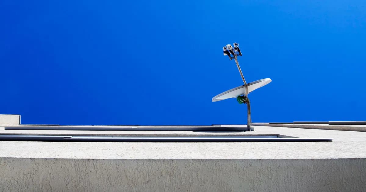 Low-angle view of a satellite dish on a modern building against a clear blue sky