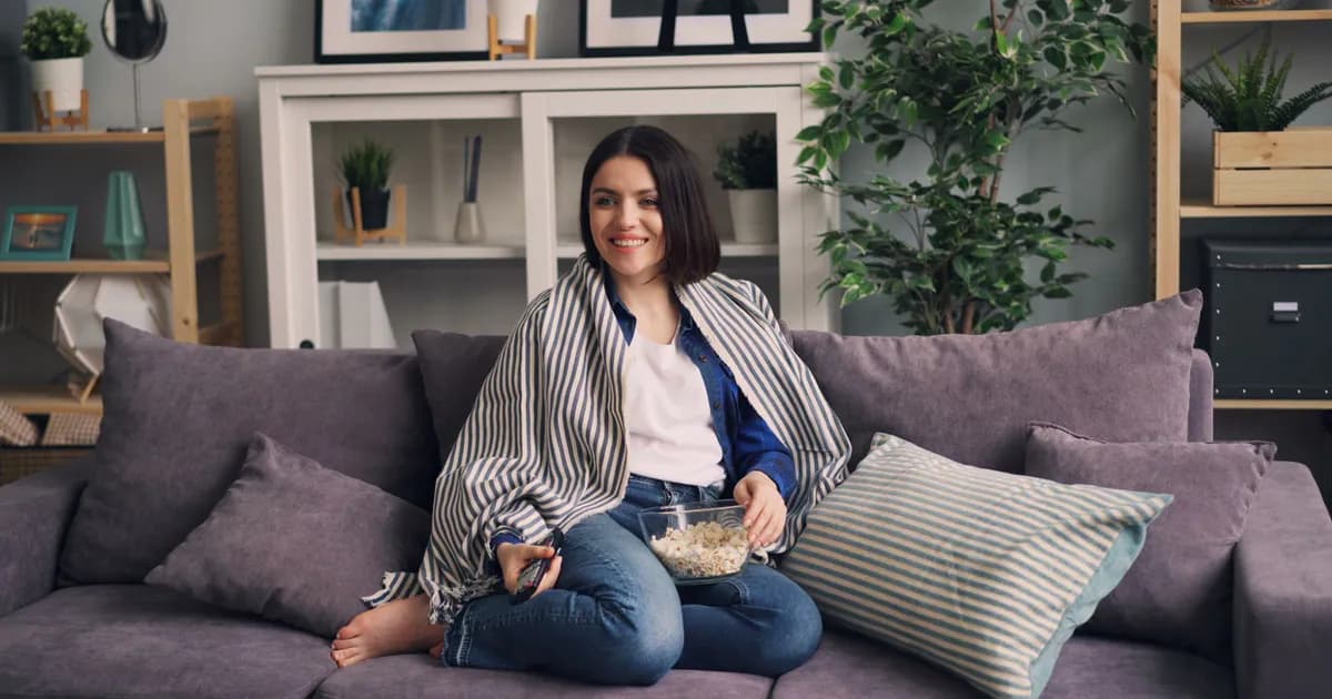 Smiling woman sitting on couch with popcorn, enjoying a cozy indoor moment