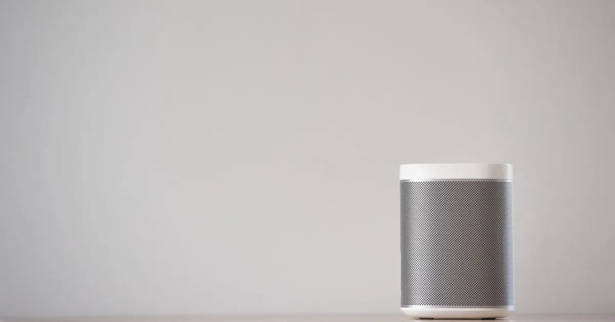 A sleek, wireless smart speaker on a wooden table against a plain wall