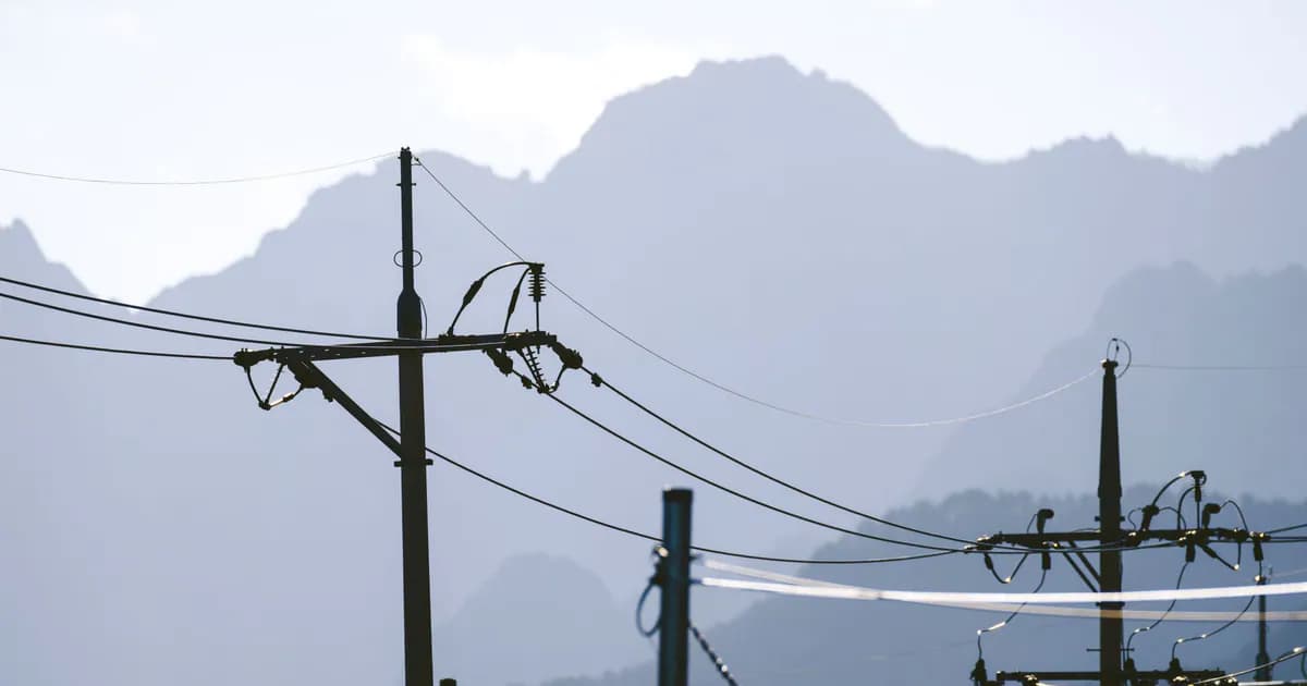 Scenic view of electric poles and wires forming silhouettes against a majestic mountain backdrop