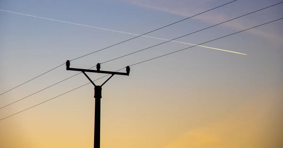 Silhouette of power lines against a colorful dusk sky with clouds and airplane contrails