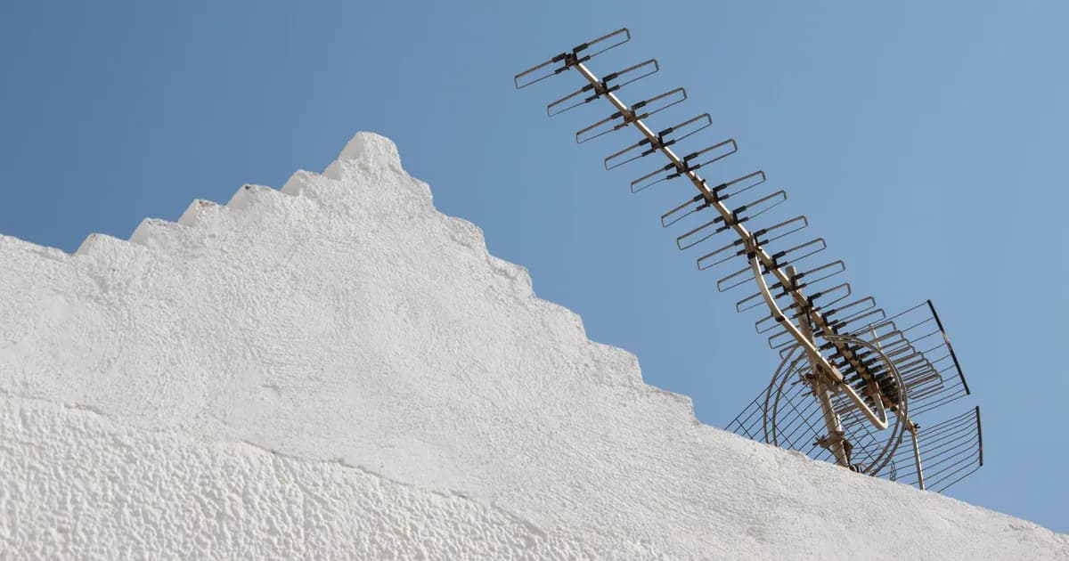 A clear view of a TV antenna atop a white building with a blue sky backdrop