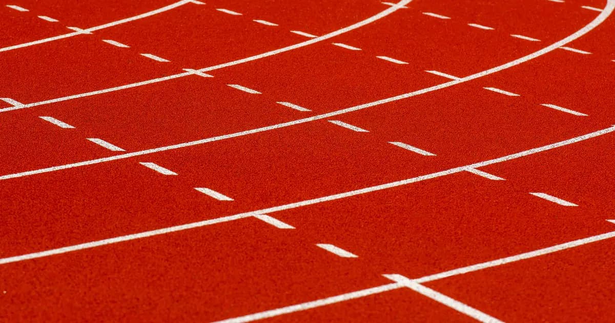 Close-up view of a curved red running track with dashed white lines for athletic sports