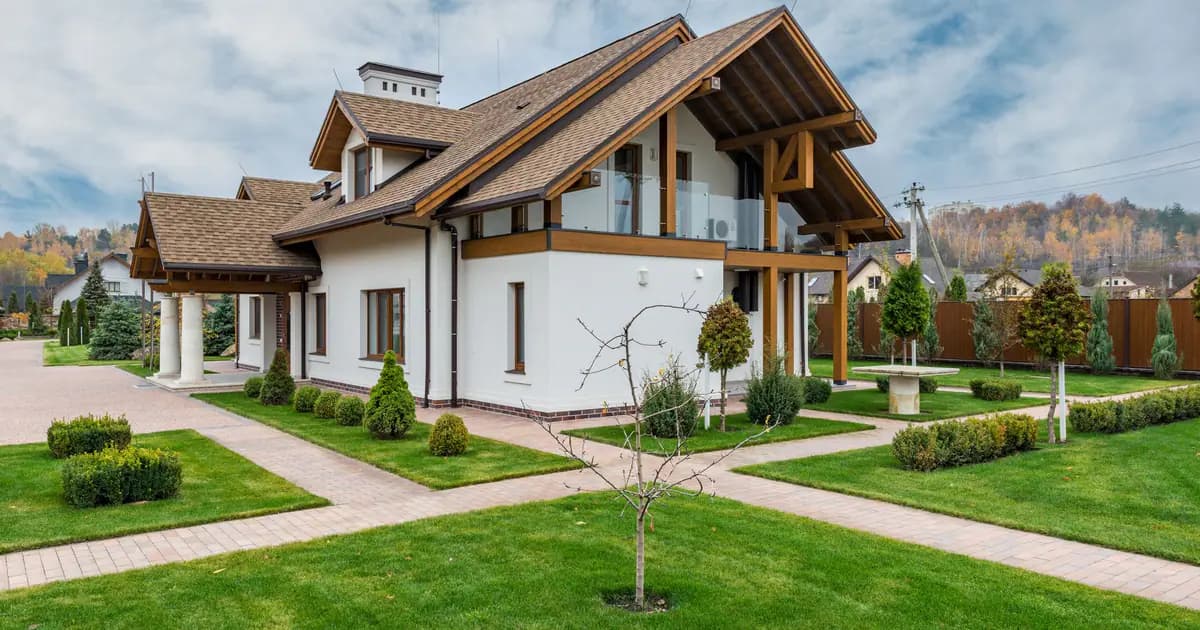 Exterior of modern cottage house with columns and balcony surrounded by green grass and trees