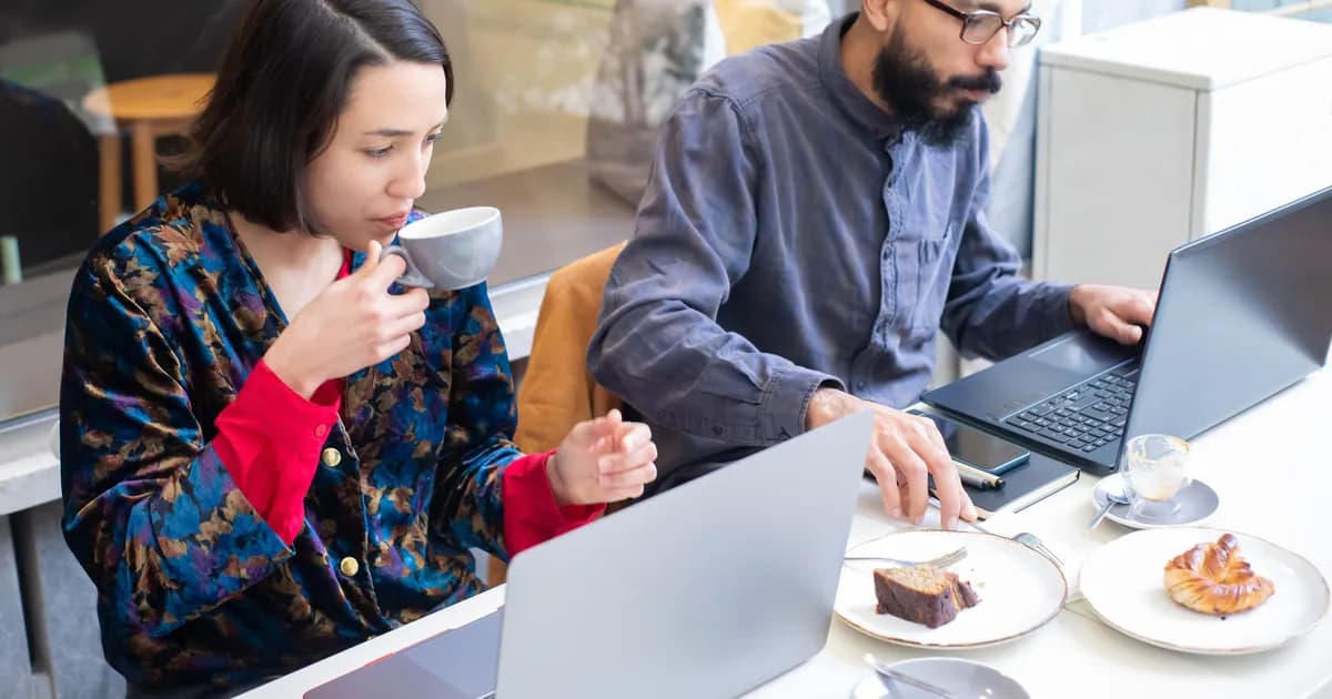Two adults working on laptops in a contemporary café, enjoying coffee and pastries