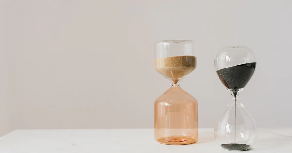 Decorative hourglasses in different shapes with pouring beige and black sand placed on white table