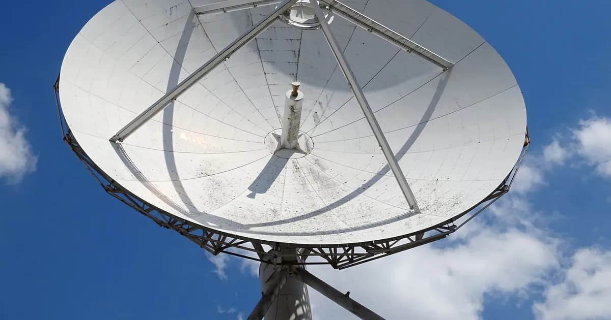 A low angle view of a large satellite dish against a clear blue sky with scattered clouds