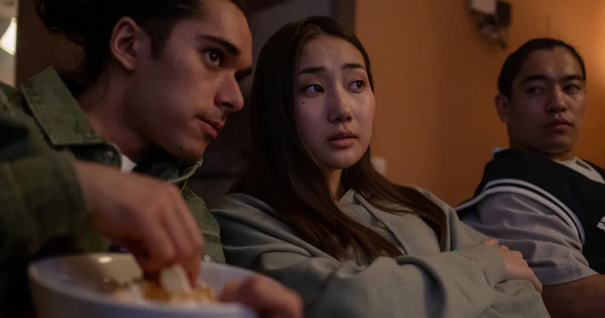Three teenagers relaxing indoors watching TV, sharing snacks during a cozy movie night