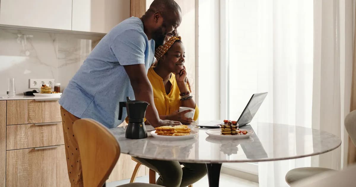 A joyful couple sharing breakfast and working on a laptop in their cozy kitchen