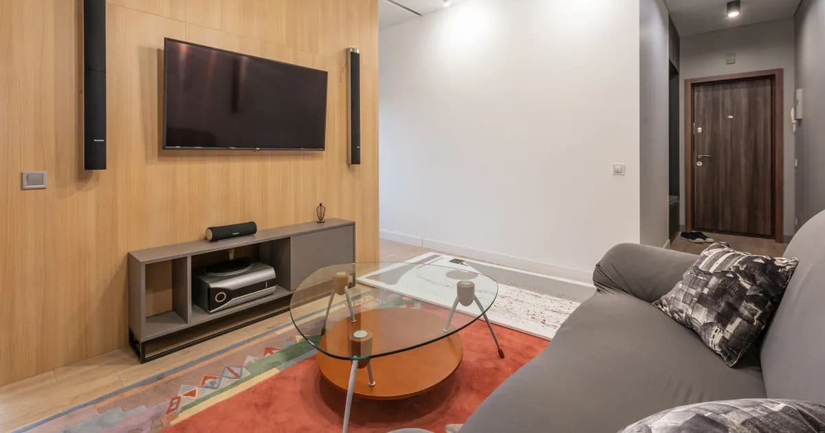 Interior of contemporary light apartment with couch with pillows near table on carpet and cabinet with TV on wall
