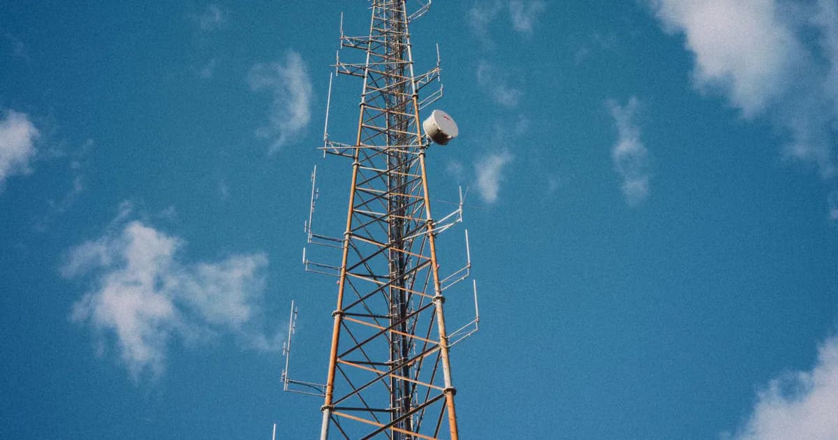 Vertical communication tower reaching into a bright blue sky with scattered clouds