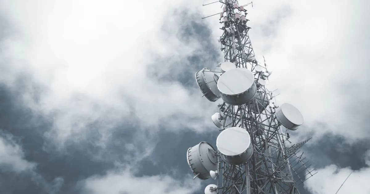 A towering communication mast with satellite dishes, set against a cloudy sky