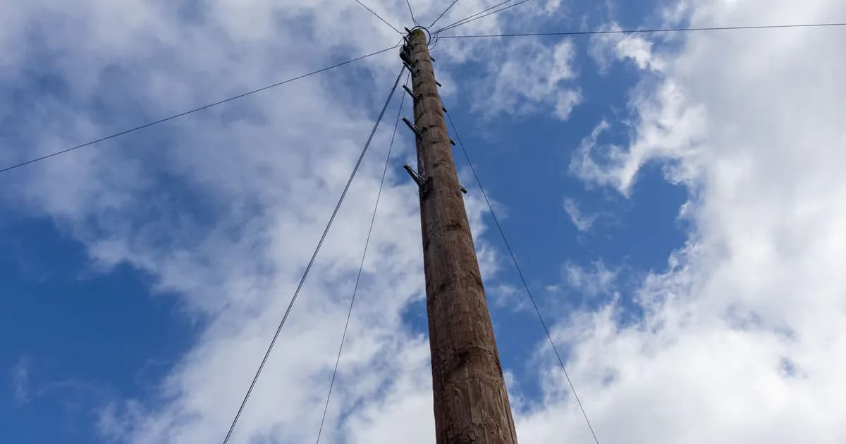Wooden utility pole with wires extending in a cloud-dappled blue sky