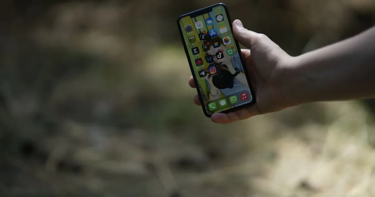 A close-up image of a hand holding a smartphone outdoors