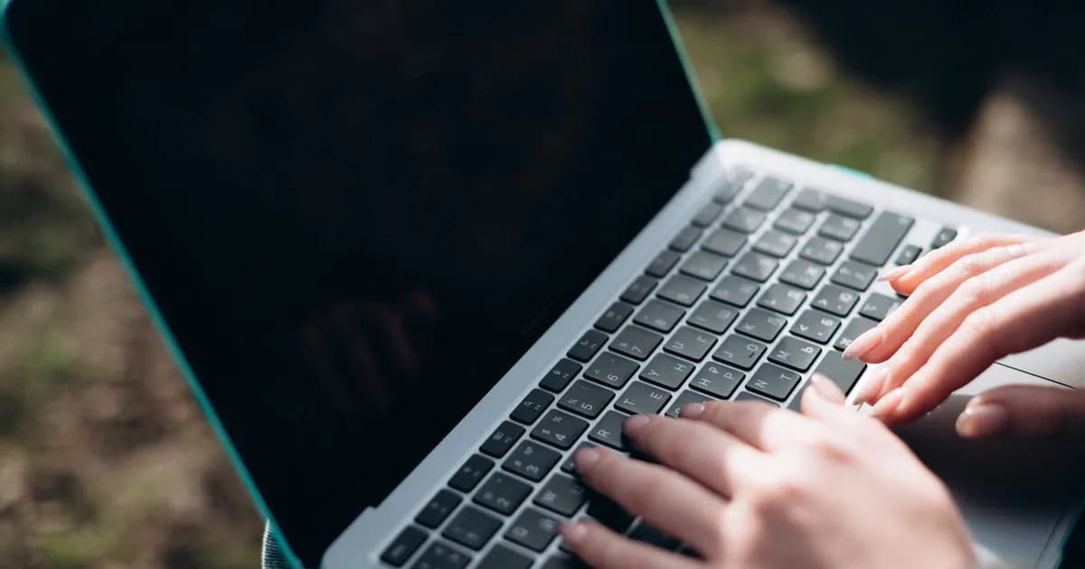 Close-up of hands typing on a laptop keyboard outdoors